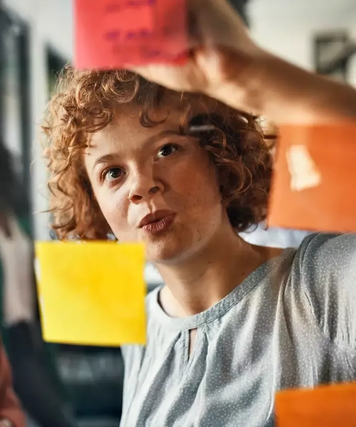Femme aux cheveux bouclés collant des notes adhésives colorées sur une vitrine